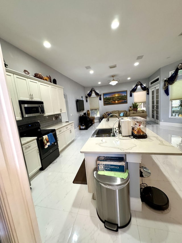 kitchen with stainless steel microwave, visible vents, black electric range oven, open floor plan, and a sink