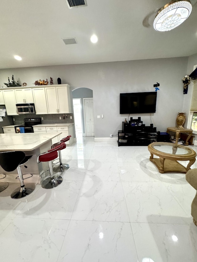 kitchen featuring arched walkways, stainless steel microwave, black electric range oven, light stone countertops, and white cabinetry