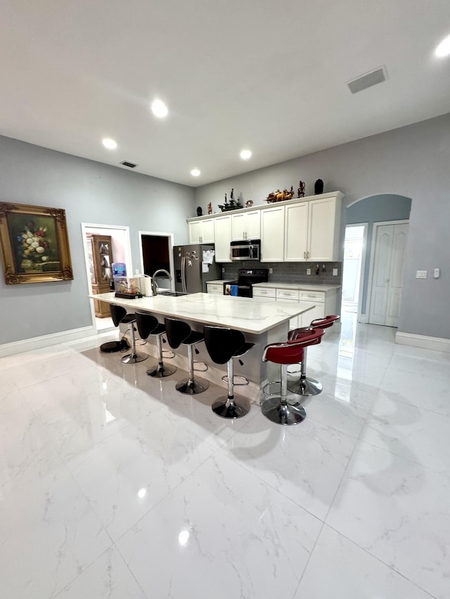 kitchen featuring arched walkways, marble finish floor, appliances with stainless steel finishes, and a kitchen bar