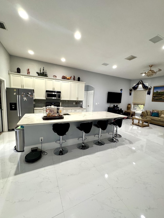 kitchen with arched walkways, marble finish floor, a breakfast bar area, appliances with stainless steel finishes, and open floor plan