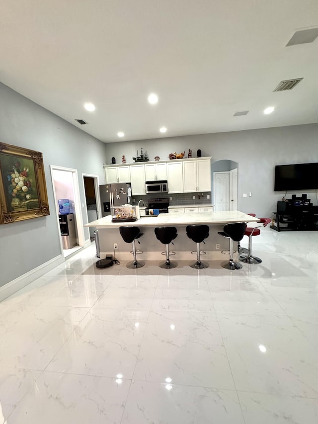 kitchen featuring arched walkways, a breakfast bar area, stainless steel appliances, visible vents, and white cabinetry