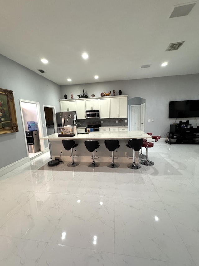 kitchen with visible vents, white cabinets, arched walkways, appliances with stainless steel finishes, and a kitchen bar