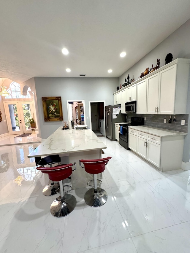 kitchen with decorative backsplash, black range with electric stovetop, freestanding refrigerator, marble finish floor, and white cabinetry