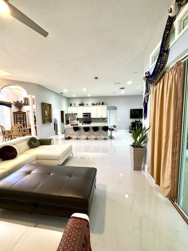 living area with arched walkways, marble finish floor, a textured ceiling, and recessed lighting