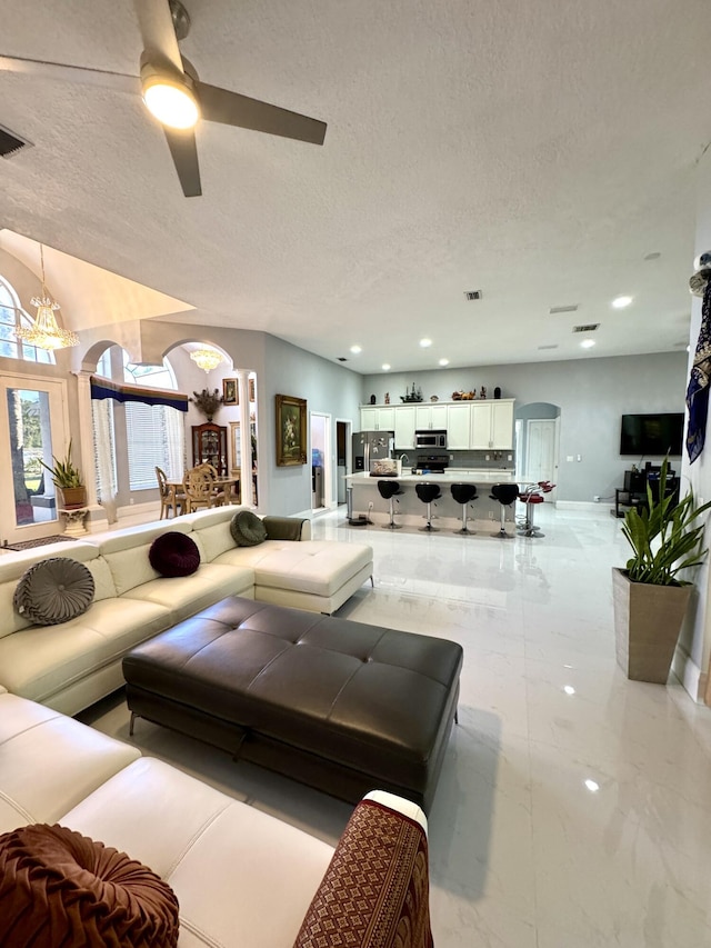 living room featuring marble finish floor, visible vents, arched walkways, and a textured ceiling