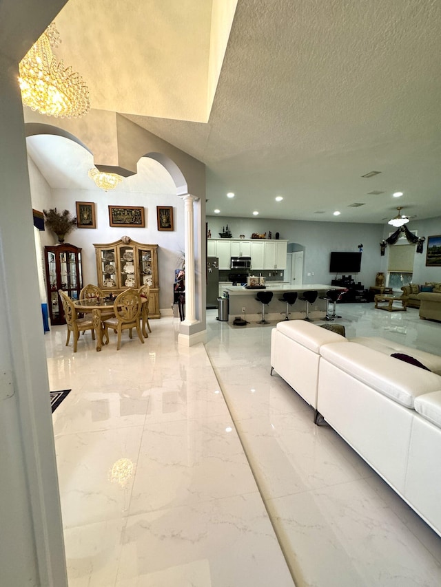 living area featuring arched walkways, a textured ceiling, recessed lighting, marble finish floor, and ornate columns