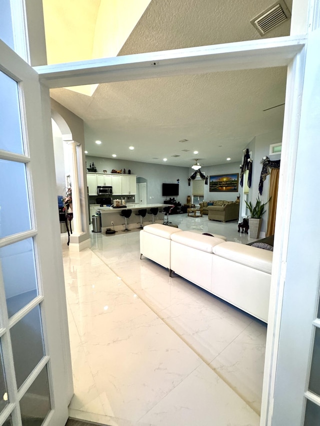 living room with visible vents, arched walkways, marble finish floor, a textured ceiling, and recessed lighting