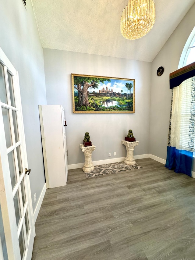 unfurnished room featuring a notable chandelier, lofted ceiling, a textured ceiling, wood finished floors, and baseboards