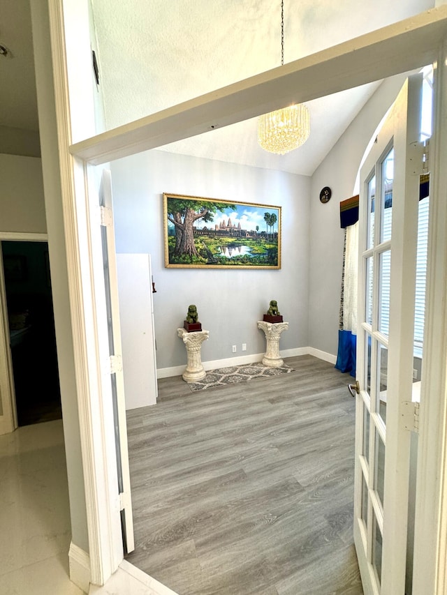 interior space with an inviting chandelier, vaulted ceiling, baseboards, and wood finished floors