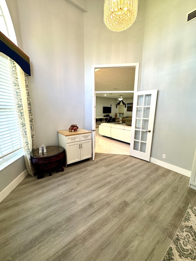 unfurnished room with a notable chandelier, visible vents, baseboards, a towering ceiling, and light wood-type flooring