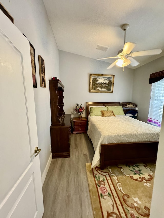 bedroom with ceiling fan, visible vents, baseboards, vaulted ceiling, and light wood finished floors