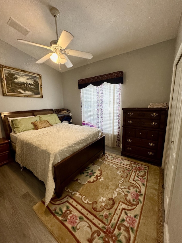 bedroom with visible vents, a ceiling fan, lofted ceiling, wood finished floors, and a textured ceiling