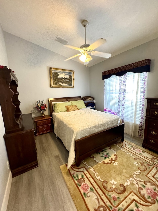 bedroom featuring visible vents, a ceiling fan, lofted ceiling, a textured ceiling, and light wood-style floors