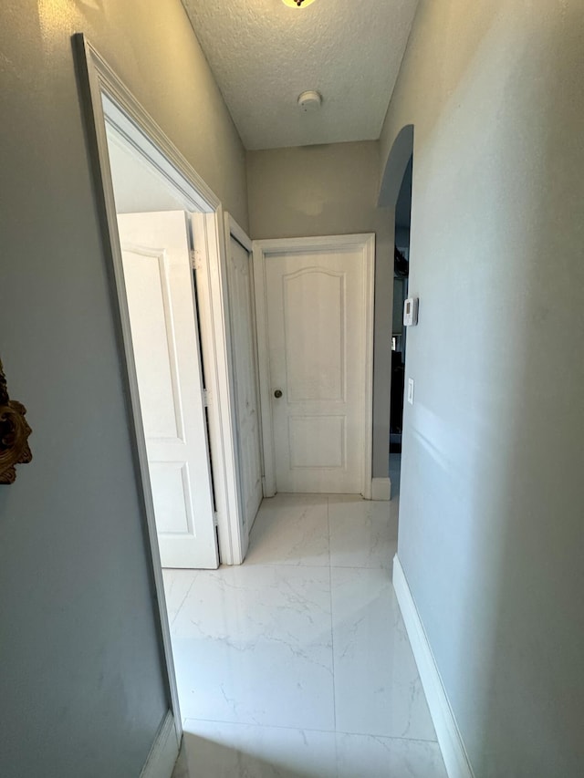 hallway featuring arched walkways, marble finish floor, a textured ceiling, and baseboards