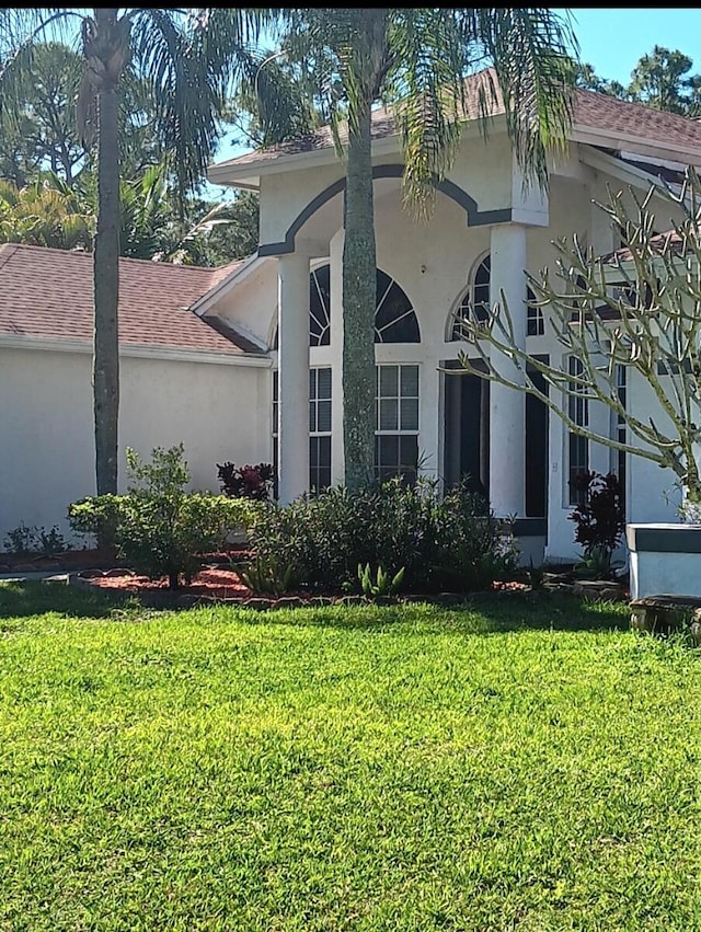 view of property exterior featuring roof with shingles, a yard, and stucco siding