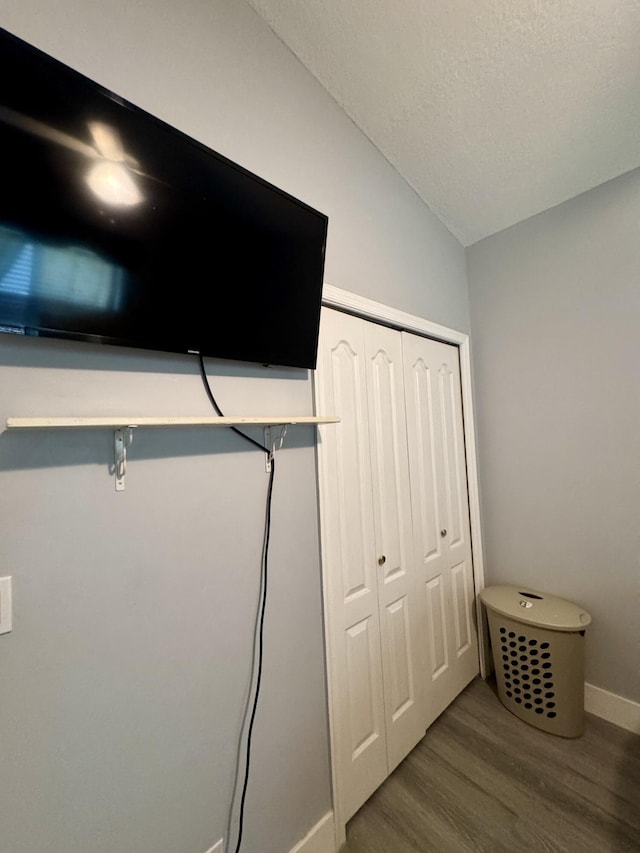 interior space with a closet, vaulted ceiling, a textured ceiling, wood finished floors, and baseboards