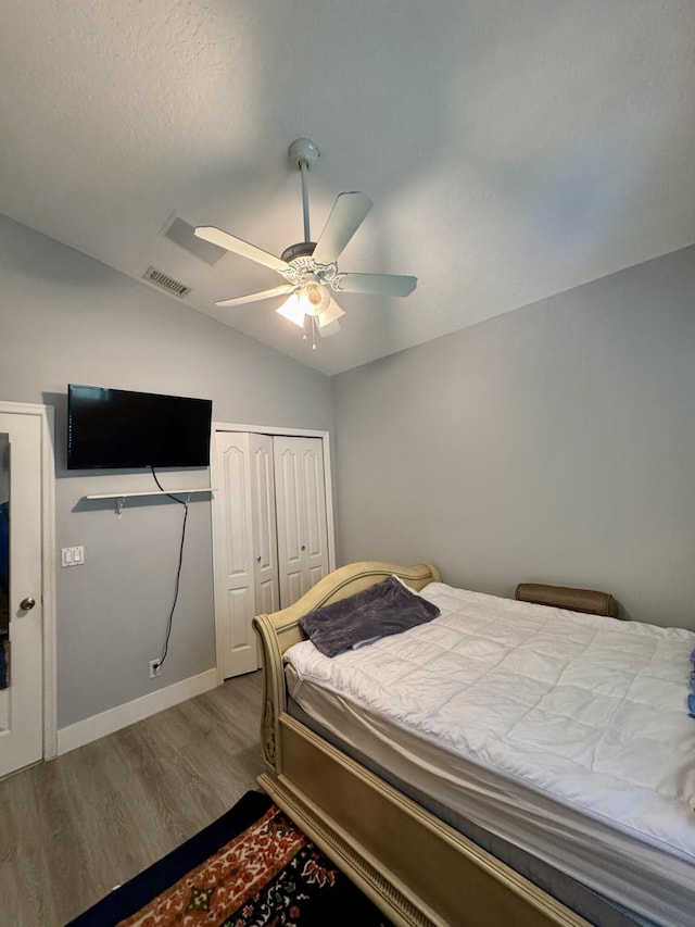 bedroom with lofted ceiling, wood finished floors, visible vents, baseboards, and a closet