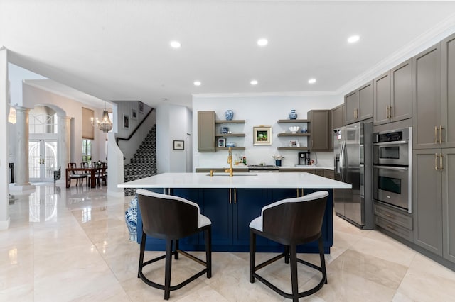 kitchen featuring a sink, appliances with stainless steel finishes, open shelves, an island with sink, and decorative columns