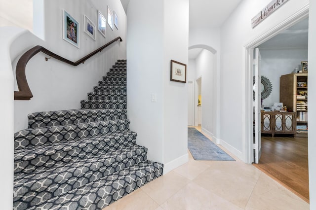 staircase featuring arched walkways, tile patterned flooring, and baseboards