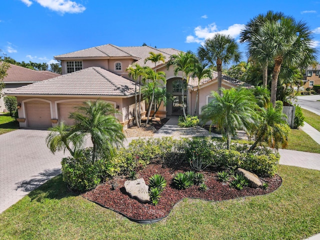 mediterranean / spanish-style house featuring an attached garage, a tile roof, decorative driveway, stucco siding, and a front yard