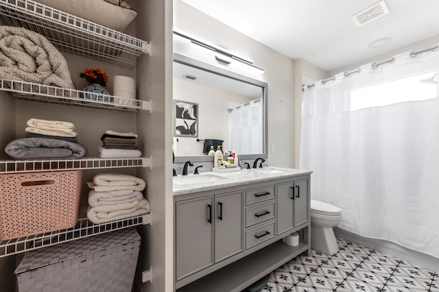 full bath featuring toilet, double vanity, visible vents, and a sink