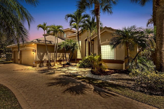 view of front of property featuring decorative driveway, an attached garage, and stucco siding