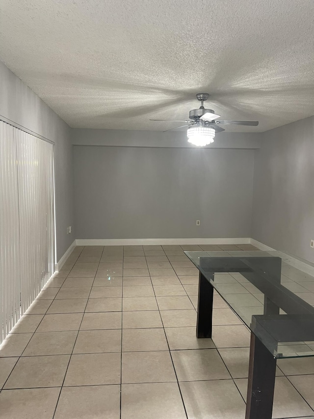 unfurnished room featuring light tile patterned floors, ceiling fan, a textured ceiling, and baseboards