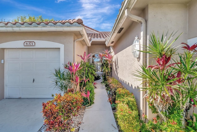 property entrance featuring a garage, a tile roof, and stucco siding