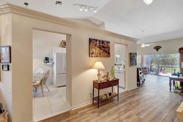 hall featuring rail lighting, visible vents, light wood-style flooring, vaulted ceiling, and baseboards