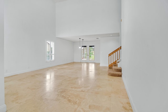 unfurnished living room featuring french doors, stairway, a towering ceiling, ornamental molding, and baseboards