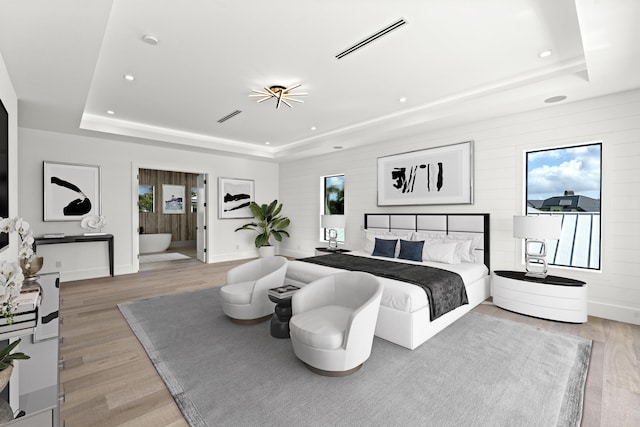 bedroom featuring a tray ceiling, light wood-style flooring, baseboards, and visible vents