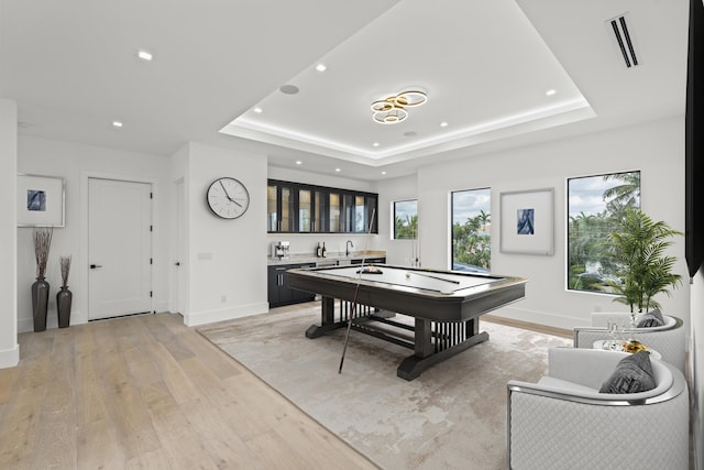 game room featuring wet bar, a raised ceiling, light wood-style floors, and visible vents