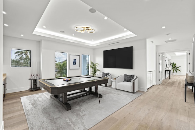 game room with a raised ceiling, light wood-style flooring, a healthy amount of sunlight, and baseboards