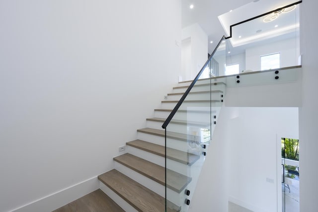 stairs featuring wood finished floors, a healthy amount of sunlight, baseboards, and a high ceiling