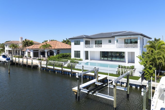 back of property featuring an outdoor pool, a water view, boat lift, and a balcony