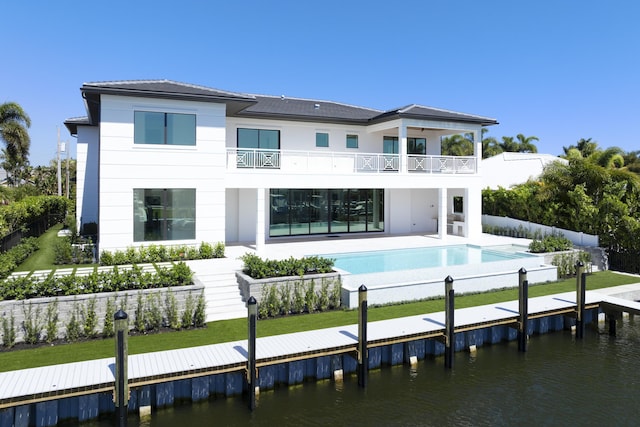 rear view of house with a balcony, a water view, fence, a yard, and a fenced in pool