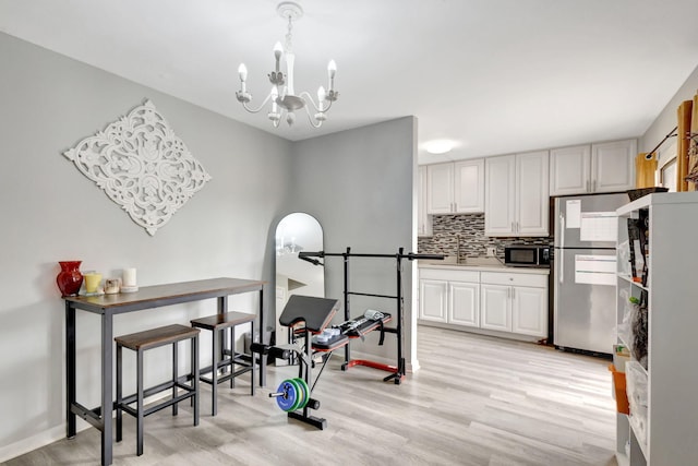 exercise room with baseboards, light wood finished floors, a sink, and an inviting chandelier