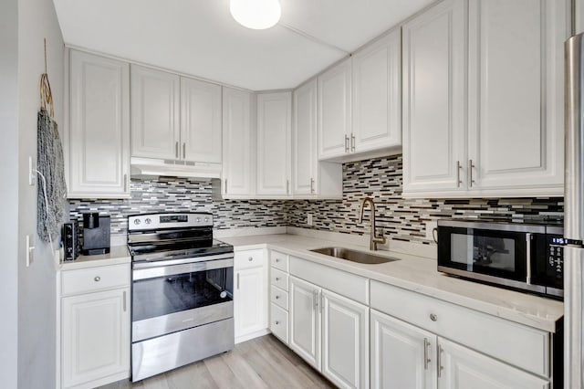 kitchen with under cabinet range hood, white cabinetry, stainless steel appliances, and a sink