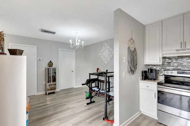 kitchen featuring light wood-style flooring, under cabinet range hood, visible vents, electric stove, and decorative backsplash