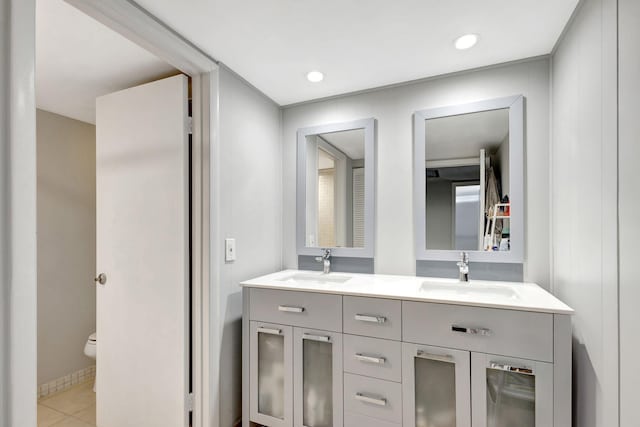 full bath featuring toilet, double vanity, a sink, and tile patterned floors