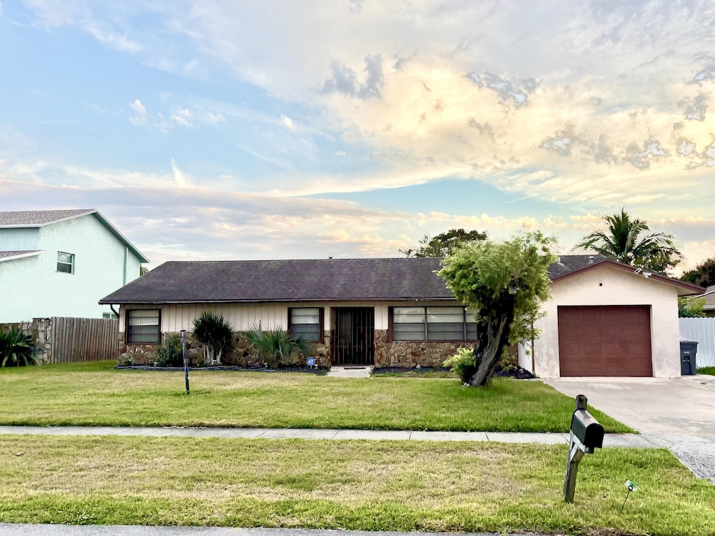 ranch-style home with a garage, driveway, fence, and a front lawn