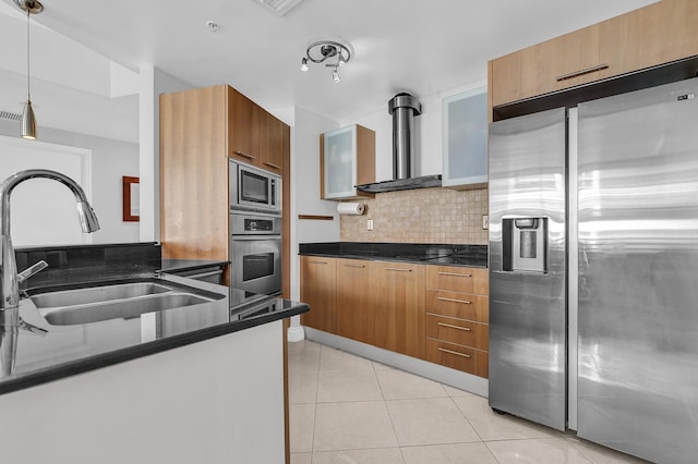 kitchen featuring dark countertops, backsplash, appliances with stainless steel finishes, wall chimney exhaust hood, and a sink