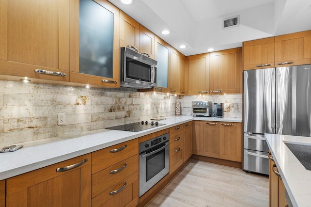 kitchen featuring light wood finished floors, visible vents, decorative backsplash, glass insert cabinets, and appliances with stainless steel finishes