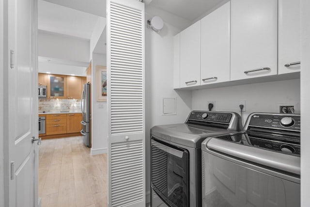 laundry area featuring light wood-type flooring, cabinet space, and washing machine and clothes dryer