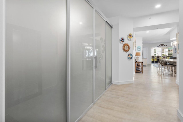 hallway featuring baseboards, light wood-type flooring, and recessed lighting