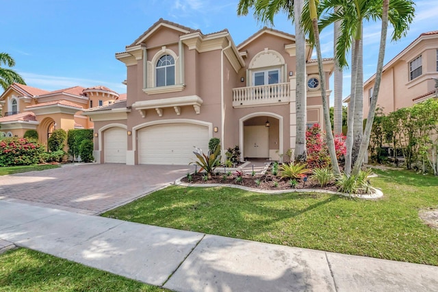 mediterranean / spanish-style home featuring an attached garage, a balcony, decorative driveway, stucco siding, and a front lawn