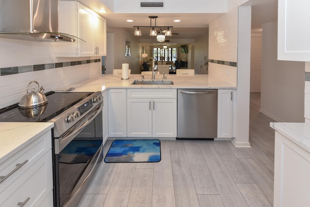 1001 Seafarer Cir Unit 102, Jupiter, FL 33477 - kitchen featuring stainless steel appliances, wall chimney exhaust hood, a sink, white cabinets, and decorative backsplash