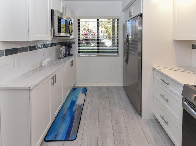1001 Seafarer Cir Unit 102, Jupiter, FL 33477 - kitchen with stainless steel appliances, white cabinets, light wood-style flooring, decorative backsplash, and baseboards