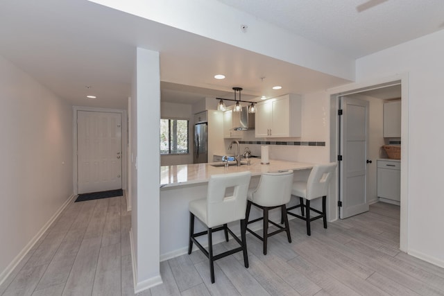 1001 Seafarer Cir Unit 102, Jupiter, FL 33477 - kitchen featuring wall chimney exhaust hood, freestanding refrigerator, light wood-style floors, a kitchen bar, and recessed lighting