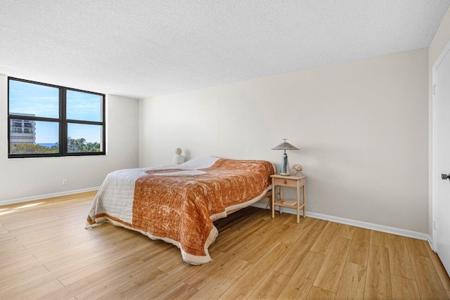 bedroom with light wood-style flooring, baseboards, and a textured ceiling